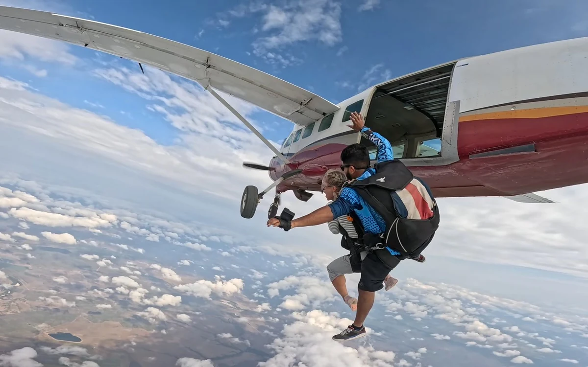 A tandem pair leaving the open door of a small aircraft above the clouds