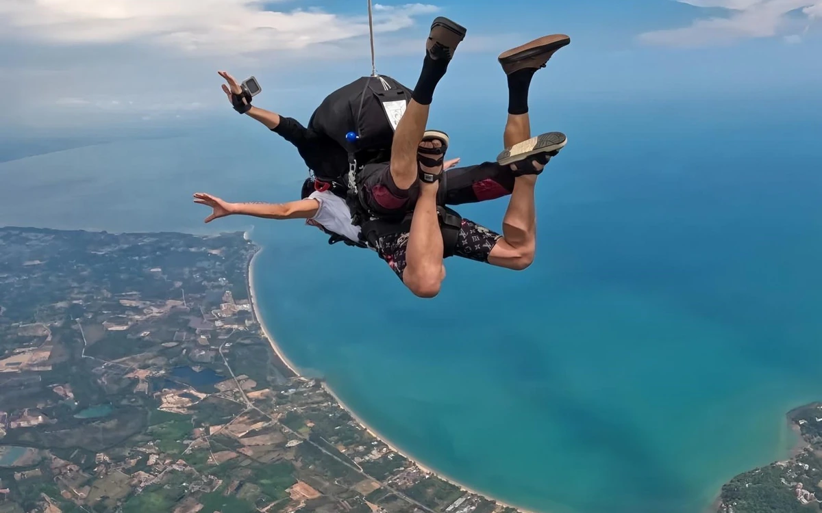 Ein Tandempaar im freien Fall über einem langen Sandstrand und einer türkisfarbenen Bucht
