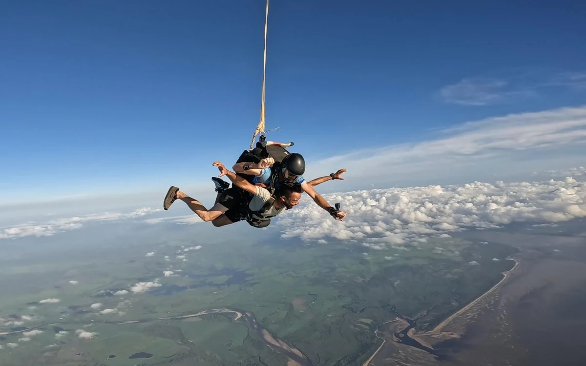 A tandem pair in freefall with green coast and tidal channels far below