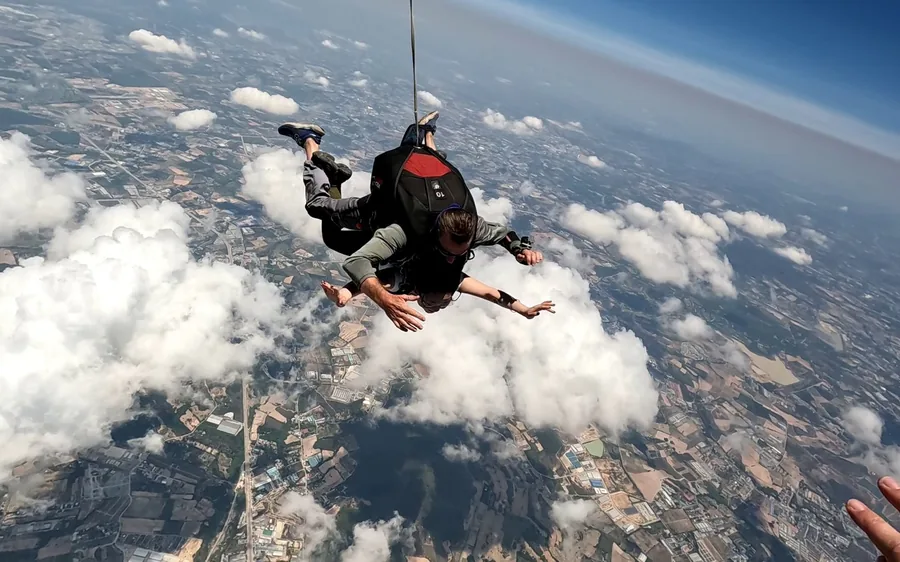 Ein Tandempaar im Freifall durch aufgelockerte Wolken, weit unter sich die Ebene