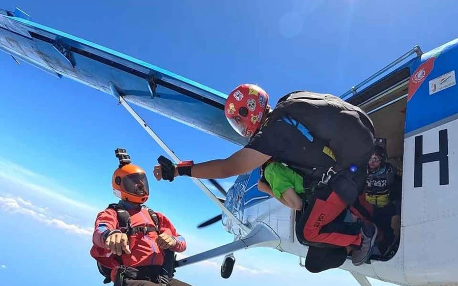 Ein Springer steigt aus der offenen Tür eines Kleinflugzeugs auf die Tragflächenstrebe